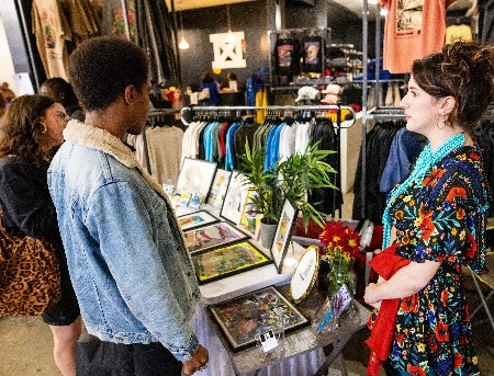 People in a shop looking at clothing merchandise and framed photos.