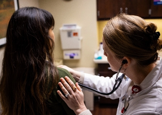 Person in white doctor's coat uses stethoscope on other person