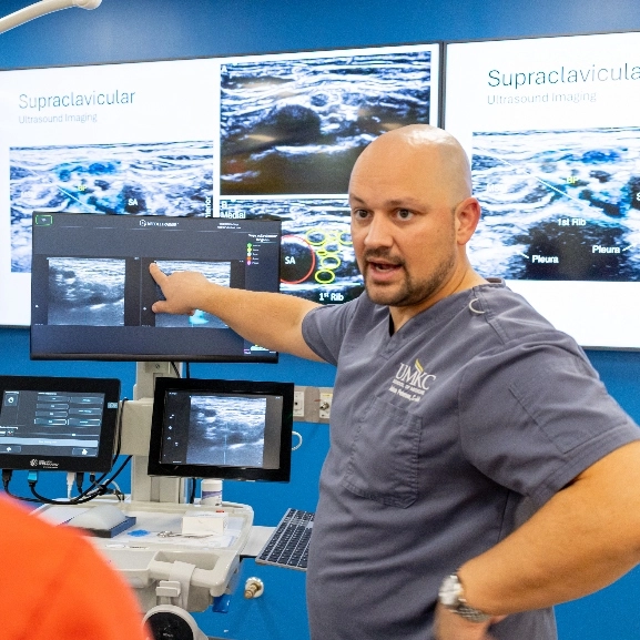 person wearing gray scrubs points to imaging monitor