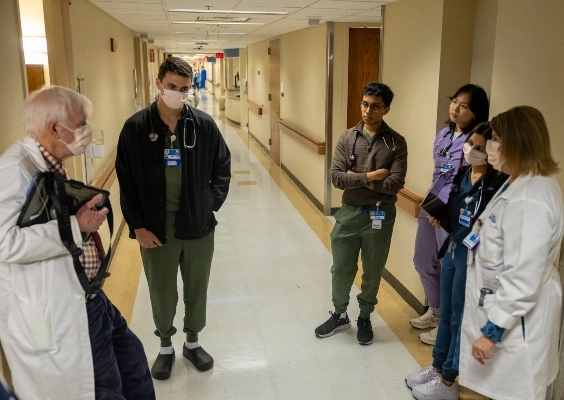 M.D. students discuss patient care with a faculty member in a hospital hallway.