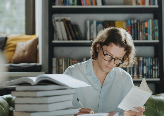 A graduate student studying with a stack of books on his desk.