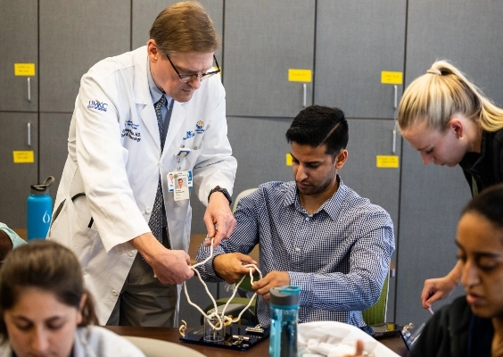 A faculty member teaching medical students how to tie sutures and knots. 