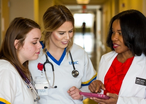 Two health sciences students and a faculty member talk in a hospital hallway.