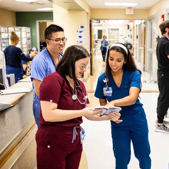 Graduate medical students and faculty talking in a hospital hallway.