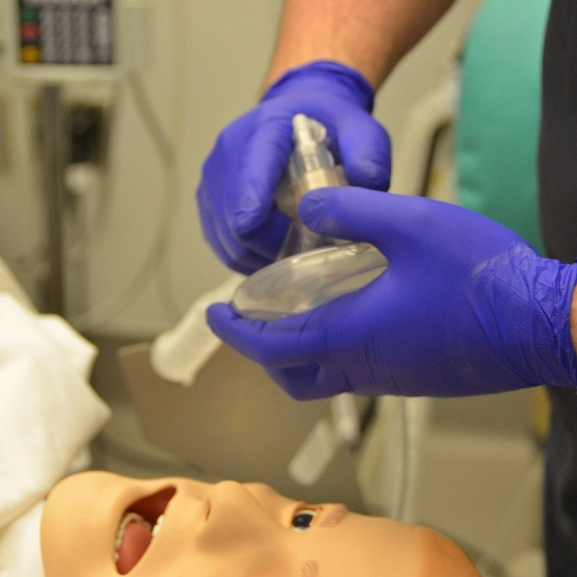 Closeup of an instructor's hands as they get ready to put a mouthpiece on a simulated patient in the simulation lab.