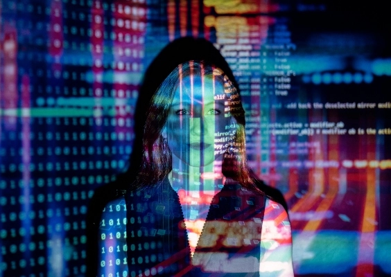 A woman standing in a dark room with bright data being projected across her face.