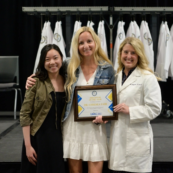 A PA students poses with her friend and a faculty member after receiving her degree during the PA White Coat ceremony.