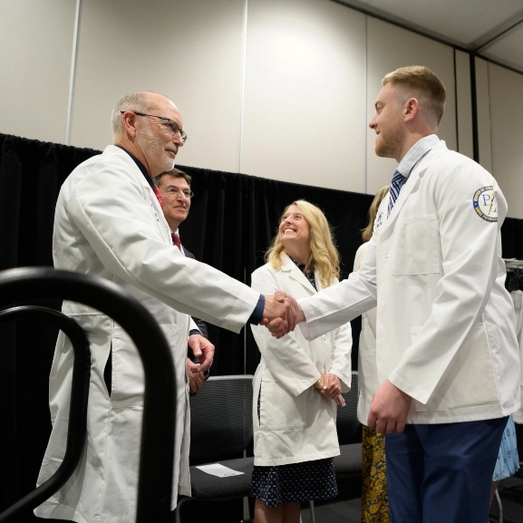 A PA student and faculty member shake hands during the PA White Coat ceremony.