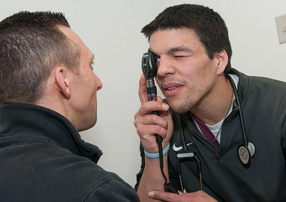 A PA students checks the eyes of a patient during an exam.