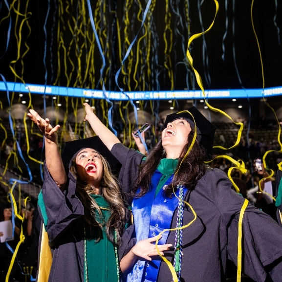 Two School of Medicine graduates celebrate during the commencement ceremony as confetti streams down.