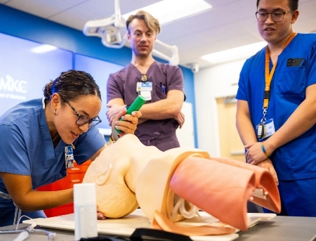 Two students practice their skills during an airway workshop while a faculty member looks on.