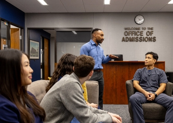 Person standing talking to people sitting with Office of Admission in background