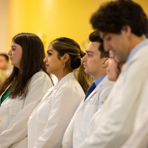 M.D. students in UMKC's rural medicine program standing as they listen to a speaker during their White Coat Ceremony.