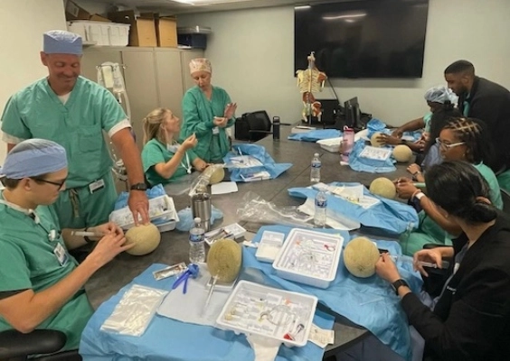 Anesthesiology residents and faculty practicing a procedure around a large conference table.