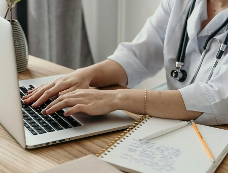 Close up of a medical student typing on their computer and taking notes.