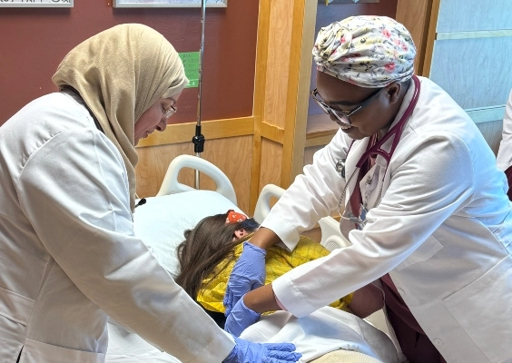 Two family medicine students helping a patient in a hospital bed.