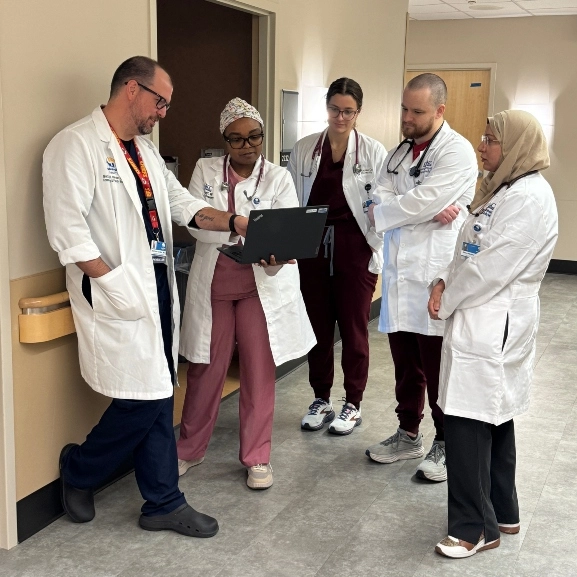 Family medicine residents and faculty talk about patient care in a hallway.