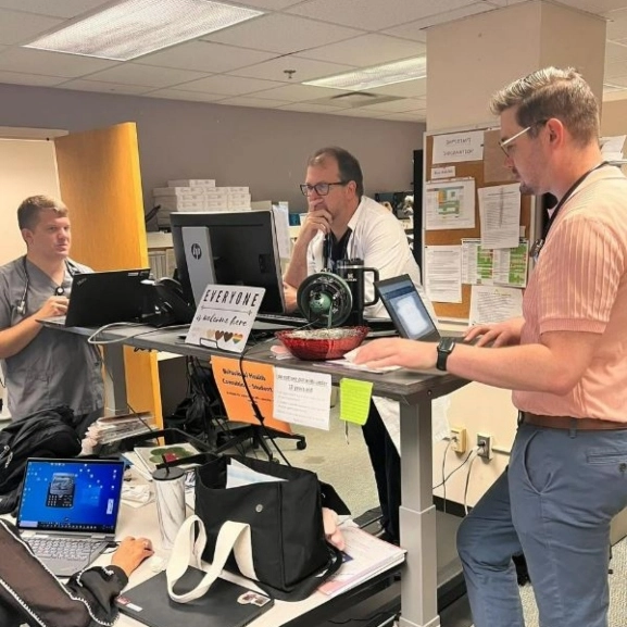 Family medicine residents and faculty stand around a hospital workstation talking about a patient case.