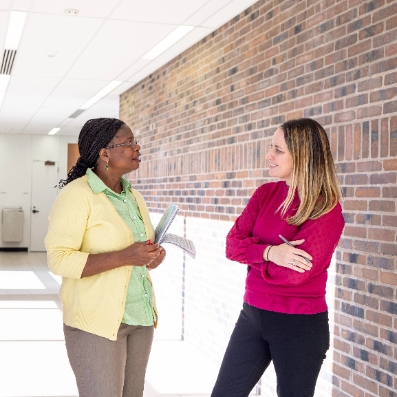 Two people stand in hallway talking