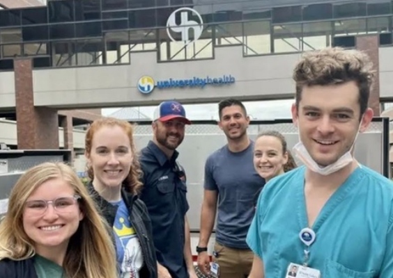 Emergency Medicine residents stand outside in front of the University Health hospital sign. 