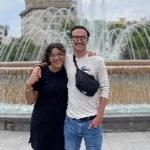 Portrait of Thomas High and his partner in front of a city fountain.