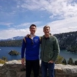 Portrait of Andrew Land standing in front of a natural landscape with a lake and forest in the background.