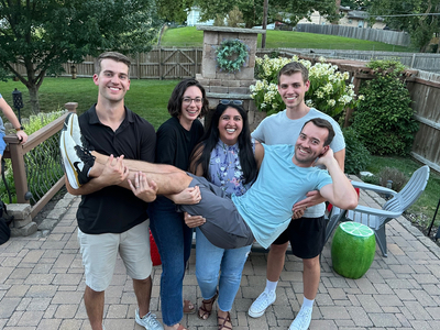 four people holding a fifth person