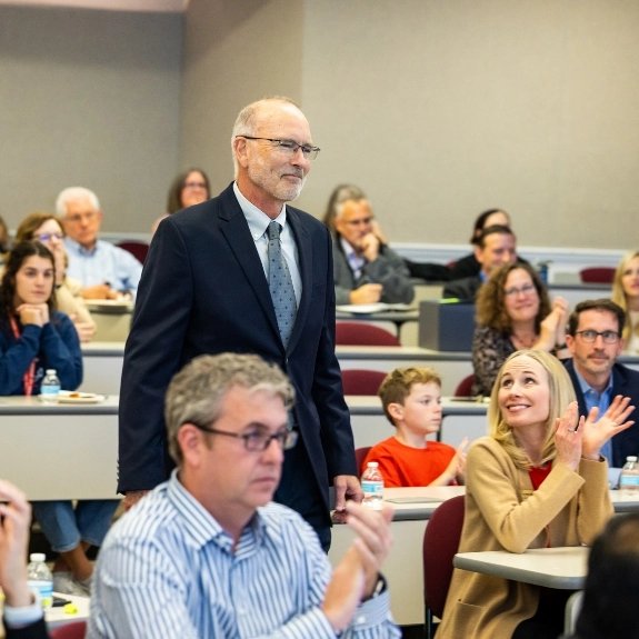 A faculty member walks towards to the podium at the faculty awards ceremony while others clap.