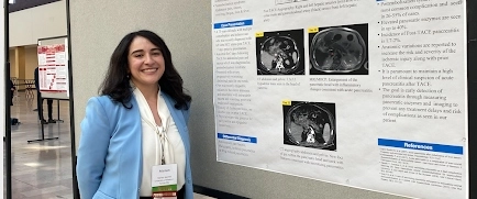 An IM resident standing in front of her presentation poster.