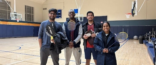 Four IM residents pose for a photo with badminton racquets inside a gym.