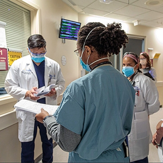 IM residents and faculty wait in a hospital hallway during rounds.