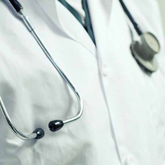 A doctor wearing their white coat with a stethoscope hanging around their shoulders.