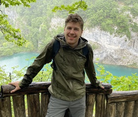 Daniel Dooling smiling during a hike that overlooks a river.