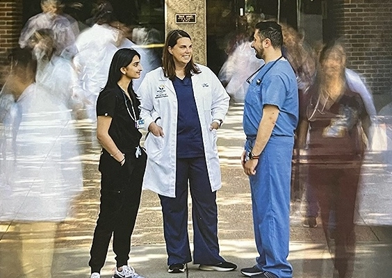 An Internal medicine and pediatrics faculty member talking with two residents outside on the Hospital Hill campus as other people walk by.