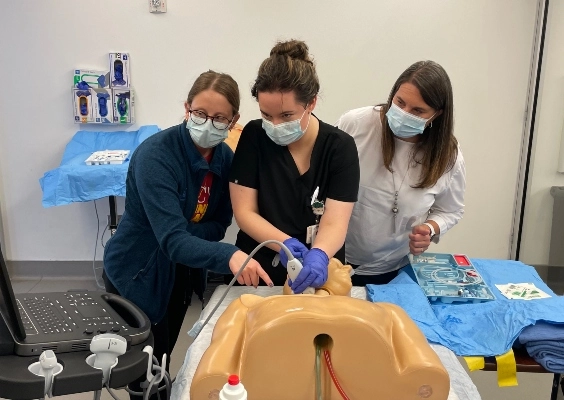 Three Medicine Pediatrics residents practice a procedure on a training dummy.