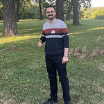 Anas standing in a grassy area with trees behind him