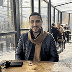 Odai sitting at a table in a glass paned room with other people at tables in the background