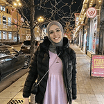 Sallam standing on the sidewalk in shopping district with holiday lightd and street lamps all around