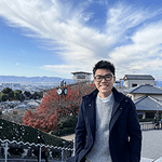 Tanawat on steps with town rooftops and a sunny sky behind him