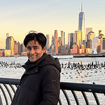  Chitramalya standing by a rail with an expansive of water and skyline behind him