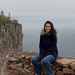 Misha sitting on stone wal with cliffs and the ocean behind her