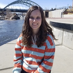 Alexandria on a river walk with the river and distant bridge behind her