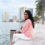 Sanjana sitting by a body of water with a skyline in the distance