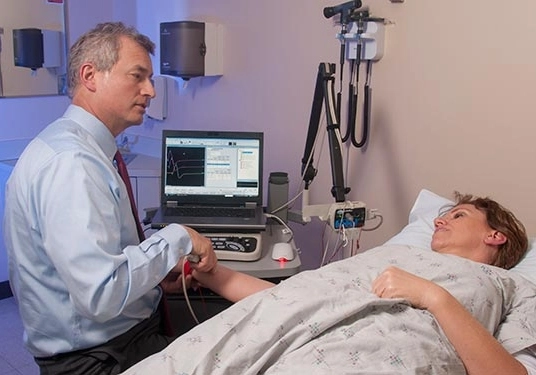 A neurologist speaking with his patient who is laying down in a medical room.