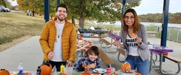 A resident smiling while carving pumpkins with a small child.