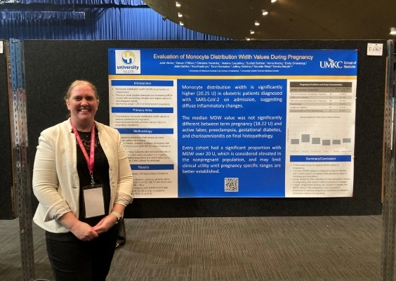 An OBGYN fellow stands next to her research poster at a conference.