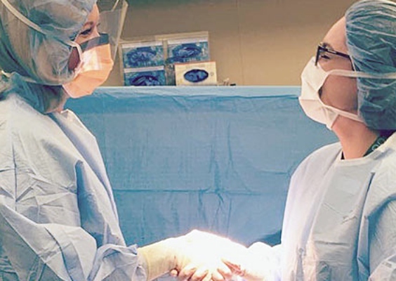 Two OBGYN residents shaking hands in a hospital room. 