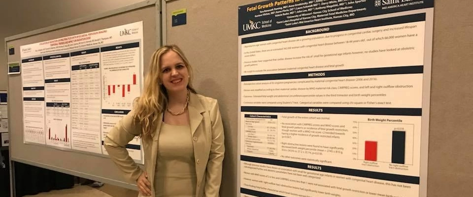 An OBGYN fellow stands next to her research poster at a conference.