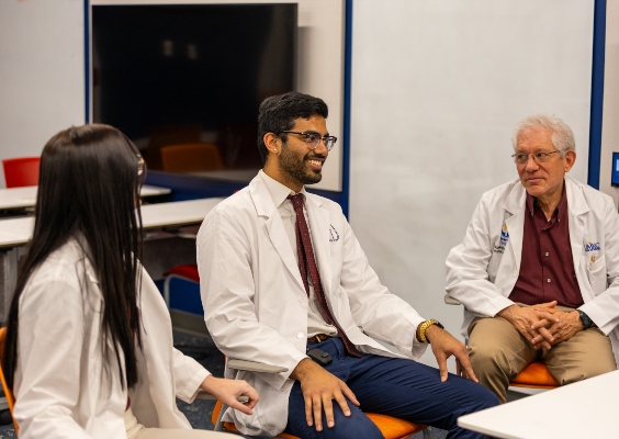 A faculty member and two medical students smiling and talking around a table.