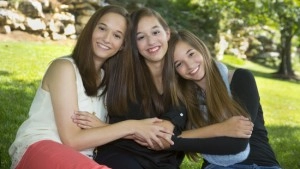 Emily Malette and her sisters smiling together in front of a beautiful landscape.